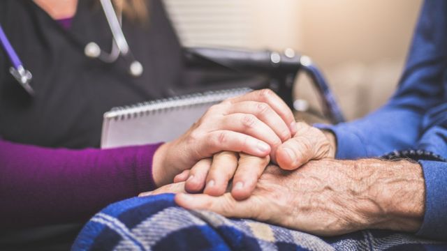 Doctora agarrando las manos de una paciente mayor