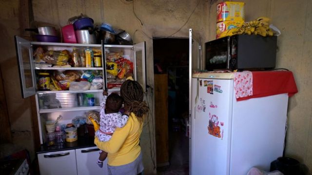 Mujer con hijo en brazos busca comida en un armario.