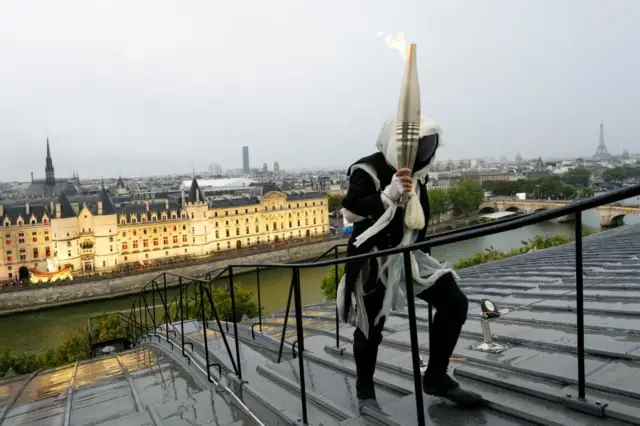 Un portador de la antorcha lleva la llama olímpica sobre un edificio a lo largo del río Sena durante la ceremonia de apertura de los Juegos Olímpicos de París 2024.