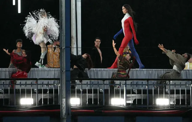 Una modelo presenta creaciones mientras camina por una pasarela erigida a lo largo del puente Passerelle Debilly sobre el río Sena durante la ceremonia de apertura de los Juegos Olímpicos de París 2024.