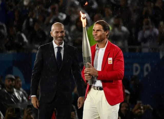 Zinedine Zidane le pasa la antorcha olímpica a Rafael Nadal.