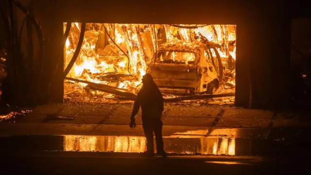 casa incendiada en california mientras. Se ve la silueta de un bombero que observa las llamas